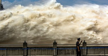 A security guard looking at his smartphone while water is released from the Three Gorges Dam, a gigantic hydropower project on the Yangtze river, to relieve flood pressure in Yichang, central China's Hubei province, July 19, 2020. (AFP Photo)
