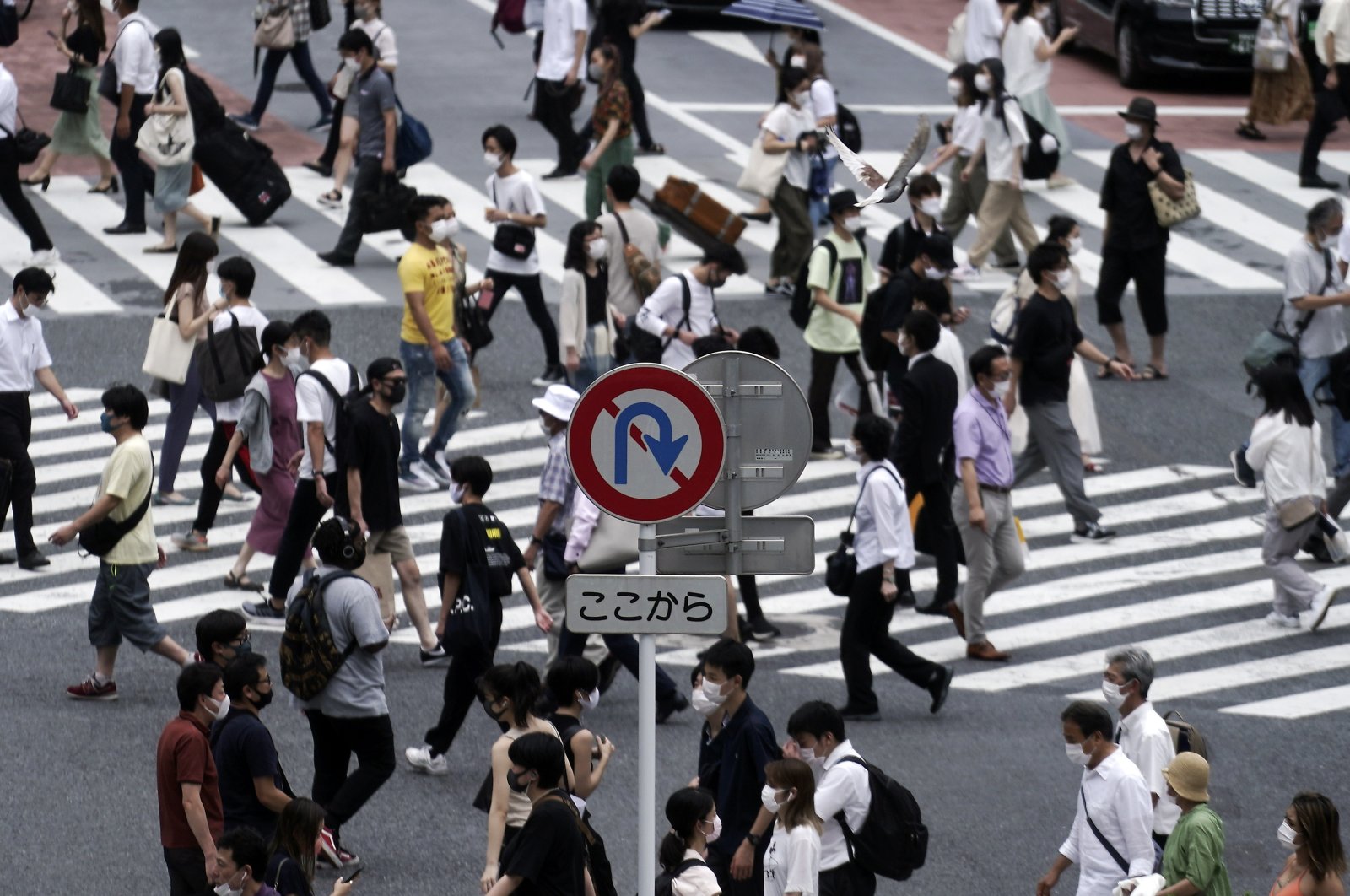 Near a No U Turn roads sign, people wearing masks against the spread of the new coronavirus walk at Shibuya pedestrian crossing in Tokyo Tuesday, July 21, 2020. (AP Photo)