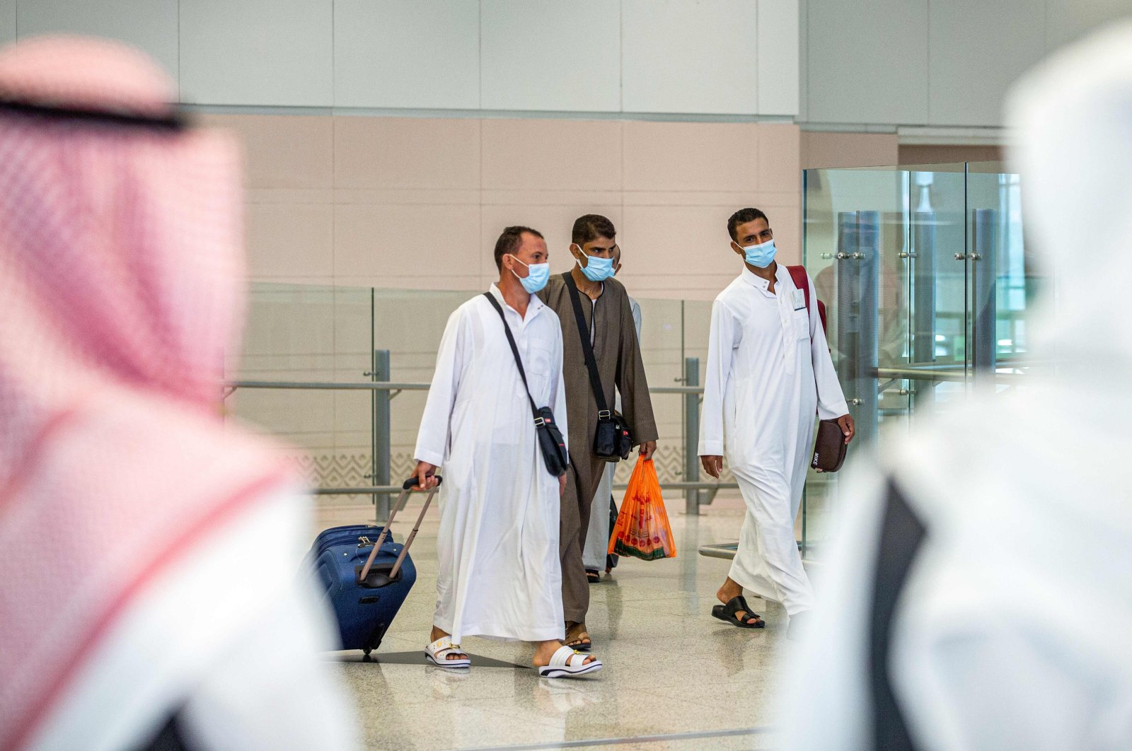 A handout picture provided by the Saudi Ministry of Hajj and Umra on July 25, 2020, shows travellers, mask-clad due to the COVID-19 coronavirus pandemic, walking with luggage as part of the first group of arrivals for the annual Hajj pilgrimage, at the Red Sea coastal city of Jeddah's King Abdulaziz International Airport.(AFP Photo)