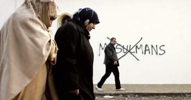 In this file photo, Muslim residents walk past racial slurs painted on the walls of a mosque in the town of Saint-Etienne in central France, Feb. 8, 2010. (Laurent Cipriani Photo via AP)
