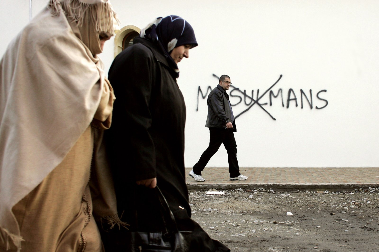 In this file photo, Muslim residents walk past racial slurs painted on the walls of a mosque in the town of Saint-Etienne in central France, Feb. 8, 2010. (Laurent Cipriani Photo via AP)