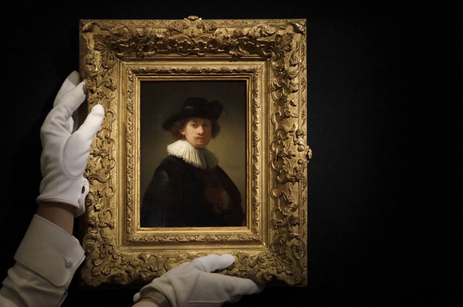 A Sotheby's employee adjusts a painting by Rembrandt Van Rijn called "Self-portrait, wearing a ruff and black hat" at Sotheby's auction rooms in London, Britain, July 23, 2020. (AP Photo)