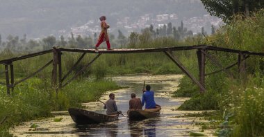A Kashmiri woman walks back home after buying bread as men row their boat after selling their vegetables at the floating vegetable market on Dal Lake in Srinagar, Indian-occupied Kashmir, July 26, 2020. (AP Photo)