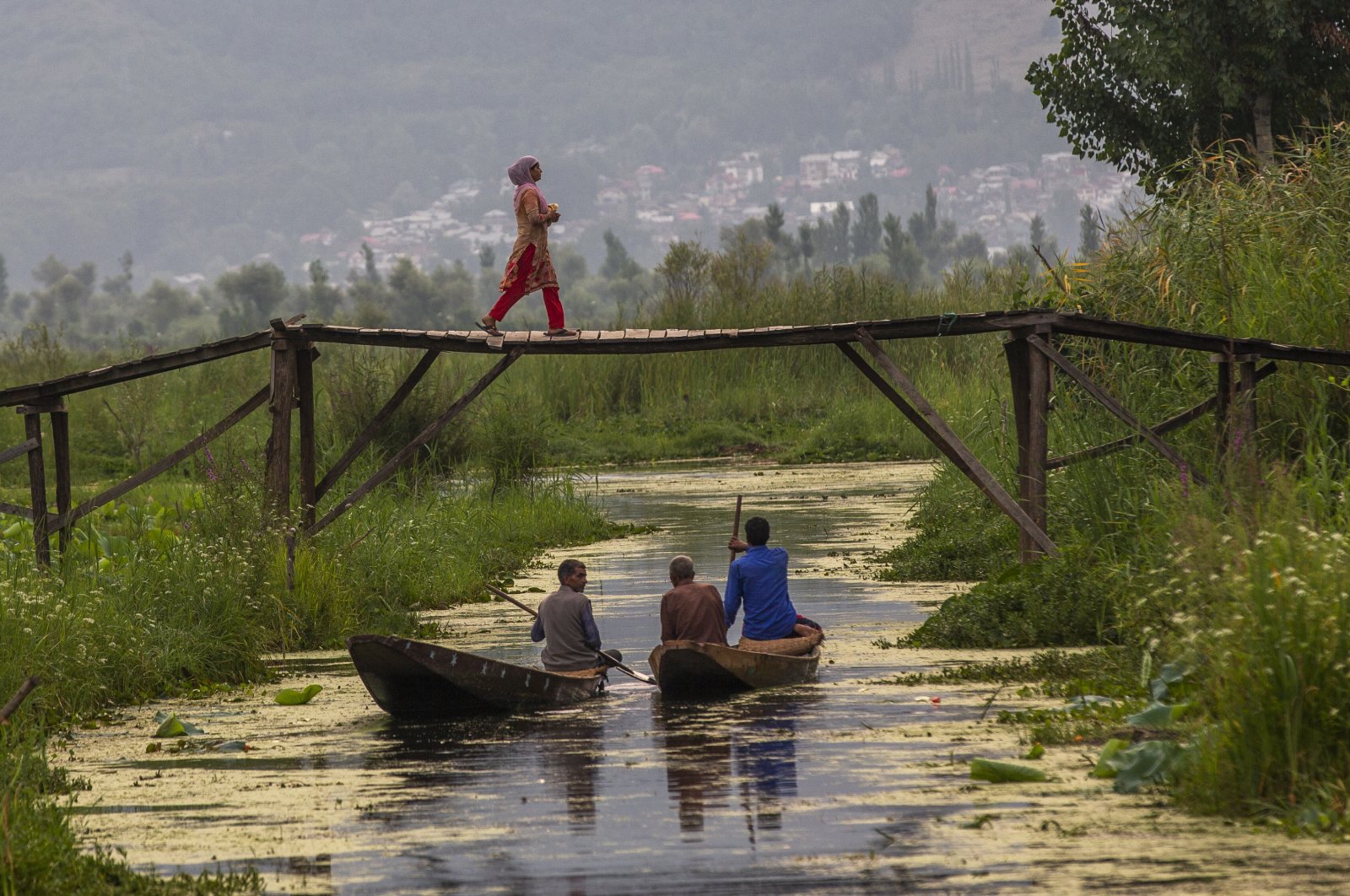 A Kashmiri woman walks back home after buying bread as men row their boat after selling their vegetables at the floating vegetable market on Dal Lake in Srinagar, Indian-occupied Kashmir, July 26, 2020. (AP Photo)