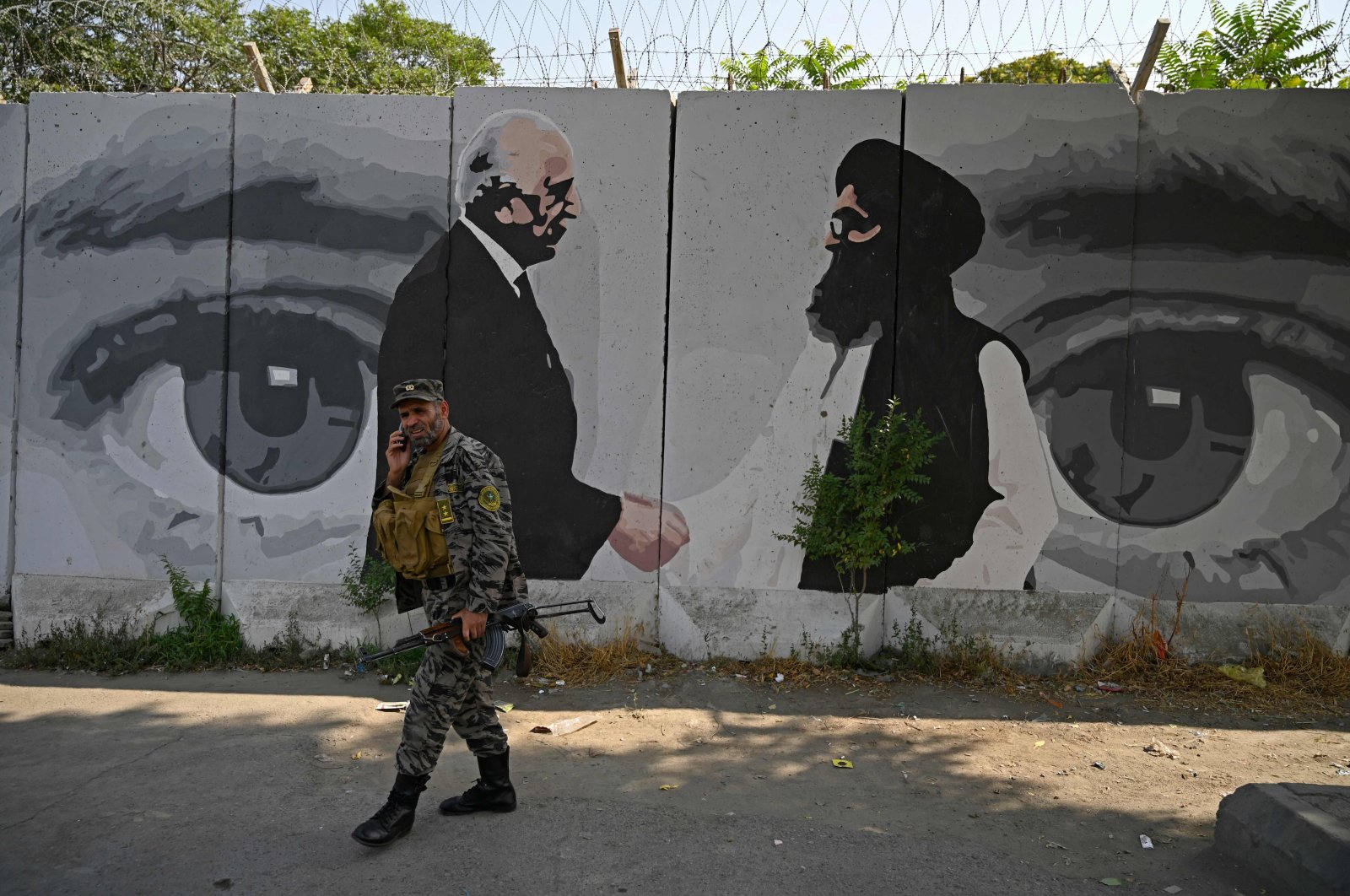 A security personnel walks past a wall mural with images of U.S. Special Representative for Afghanistan Reconciliation Zalmay Khalilzad (L) and Taliban co-founder Mullah Abdul Ghani Baradar (R), Kabul, Afghanistan, July 31, 2020. (AFP Photo)