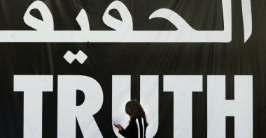A Lebanese woman uses her mobile phone as she walks past a giant banner reading "truth" in Arabic and English, Beirut, Apr. 5, 2005. (AFP Photo)