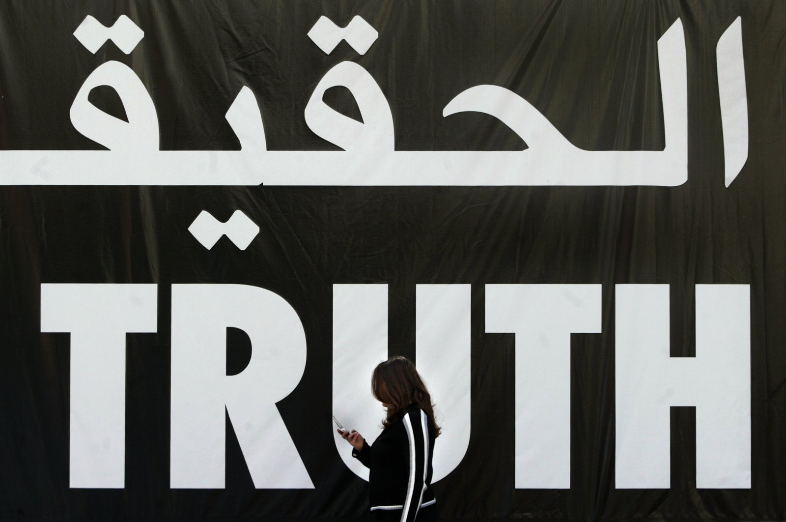 A Lebanese woman uses her mobile phone as she walks past a giant banner reading "truth" in Arabic and English, Beirut, Apr. 5, 2005. (AFP Photo)