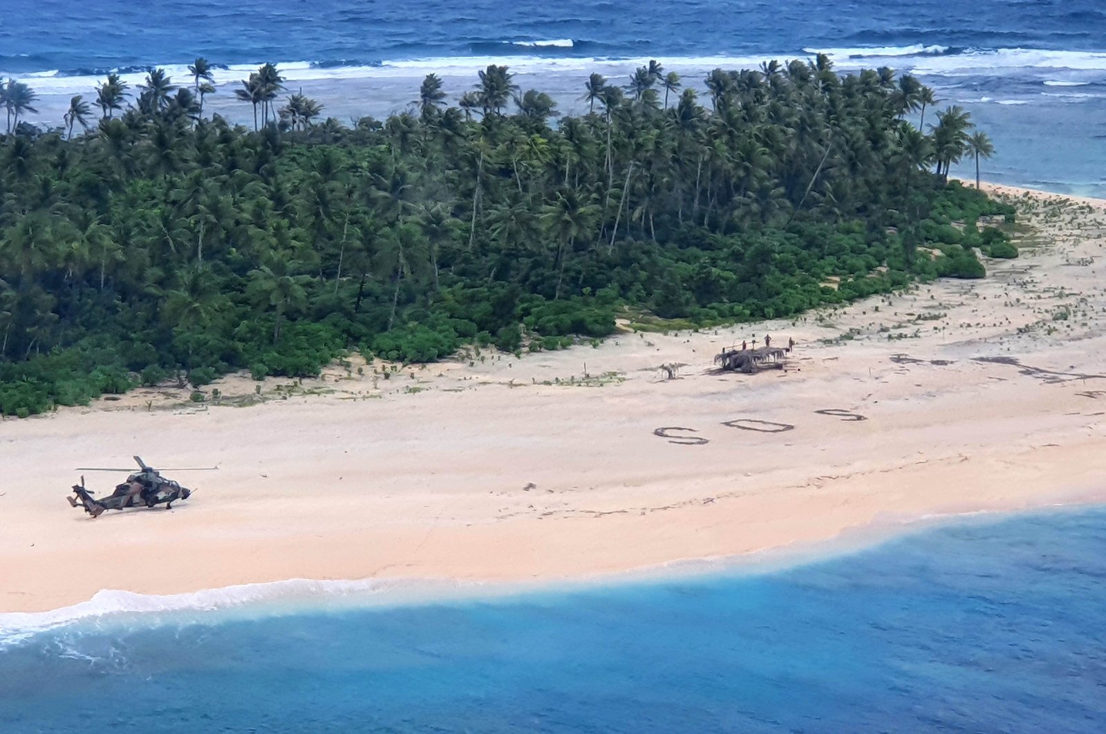 An Australian Army ARH Tiger helicopter lands near the letters "SOS" on a beach on Pikelot Island where three men were found in good condition after being missing for three days, Aug. 2, 2020. (Australian Defence Force Photo via AFP)