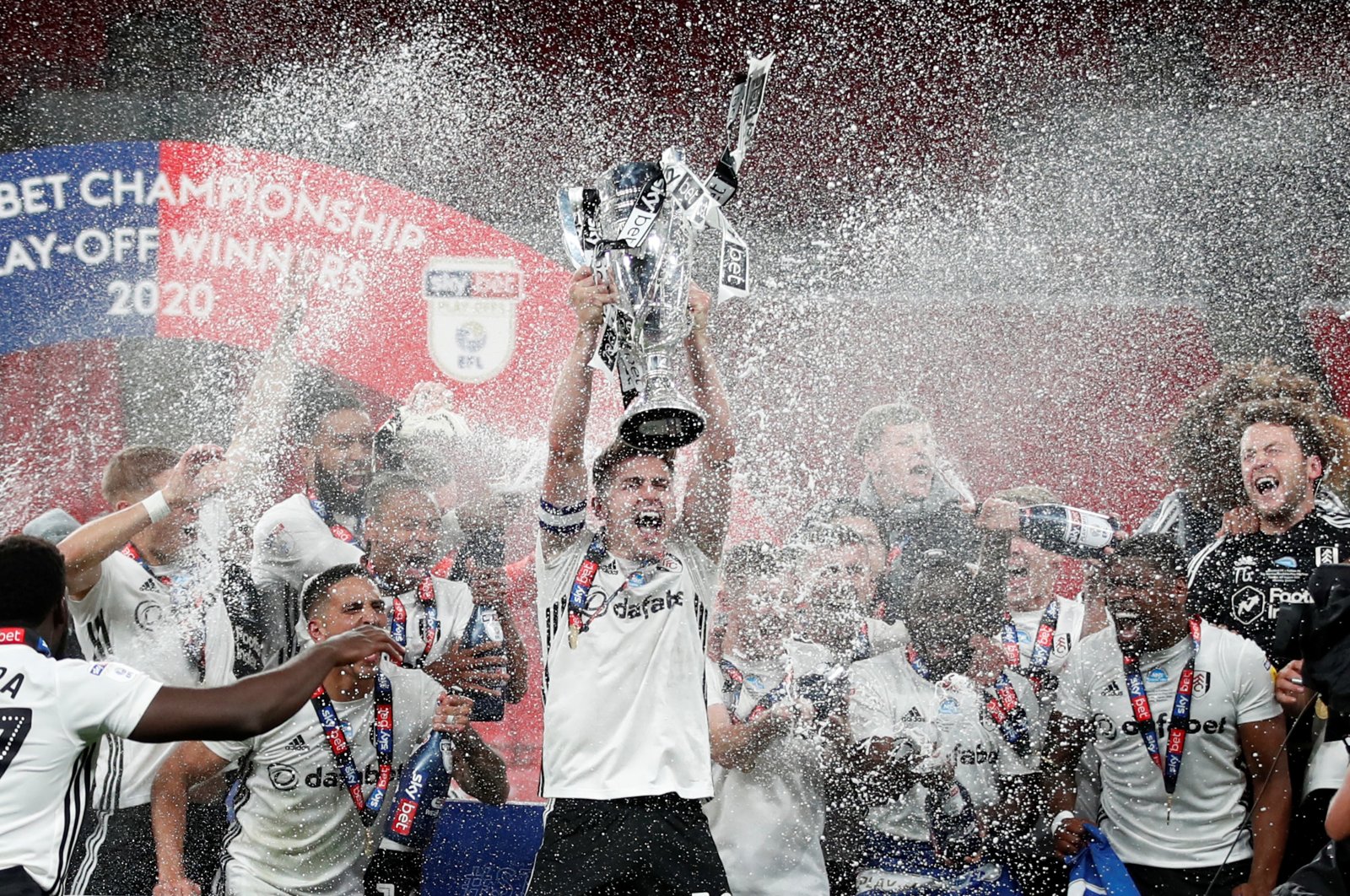 Fulham's Tom Cairney lifts EFL Championship trophy as he celebrates promotion to the Premier League with teammates after winning the playoff match against Bentford in London, Britain, Aug. 4, 2020. (Reuters Photo)