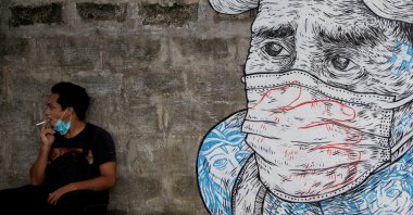 A man smokes a cigarette next to a mural of a man wearing a protective mask amid the COVID-19 outbreak in Quezon City, Metro Manila, Philippines, July 30, 2020. (REUTERS Photo)