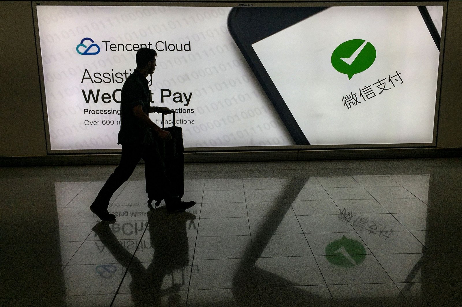 This Aug. 21, 2017 file photo shows a man walking at Hong Kong's international airport past an advertisement for the WeChat social media platform, owned by China's Tencent. (AFP Photo)