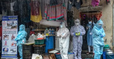 Health workers wearing personal protective equipment (PPE) suits take shelter while conducting a COVID-19 screening under heavy rain, Mumbai, India, Aug. 12, 2020. (AFP Photo)