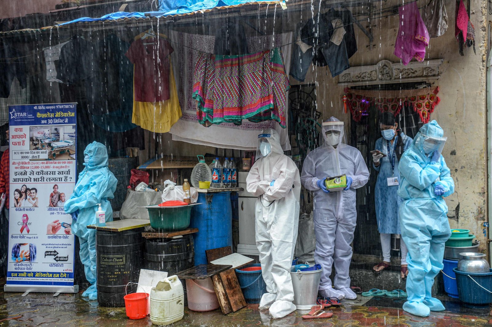 Health workers wearing personal protective equipment (PPE) suits take shelter while conducting a COVID-19 screening under heavy rain, Mumbai, India, Aug. 12, 2020. (AFP Photo)