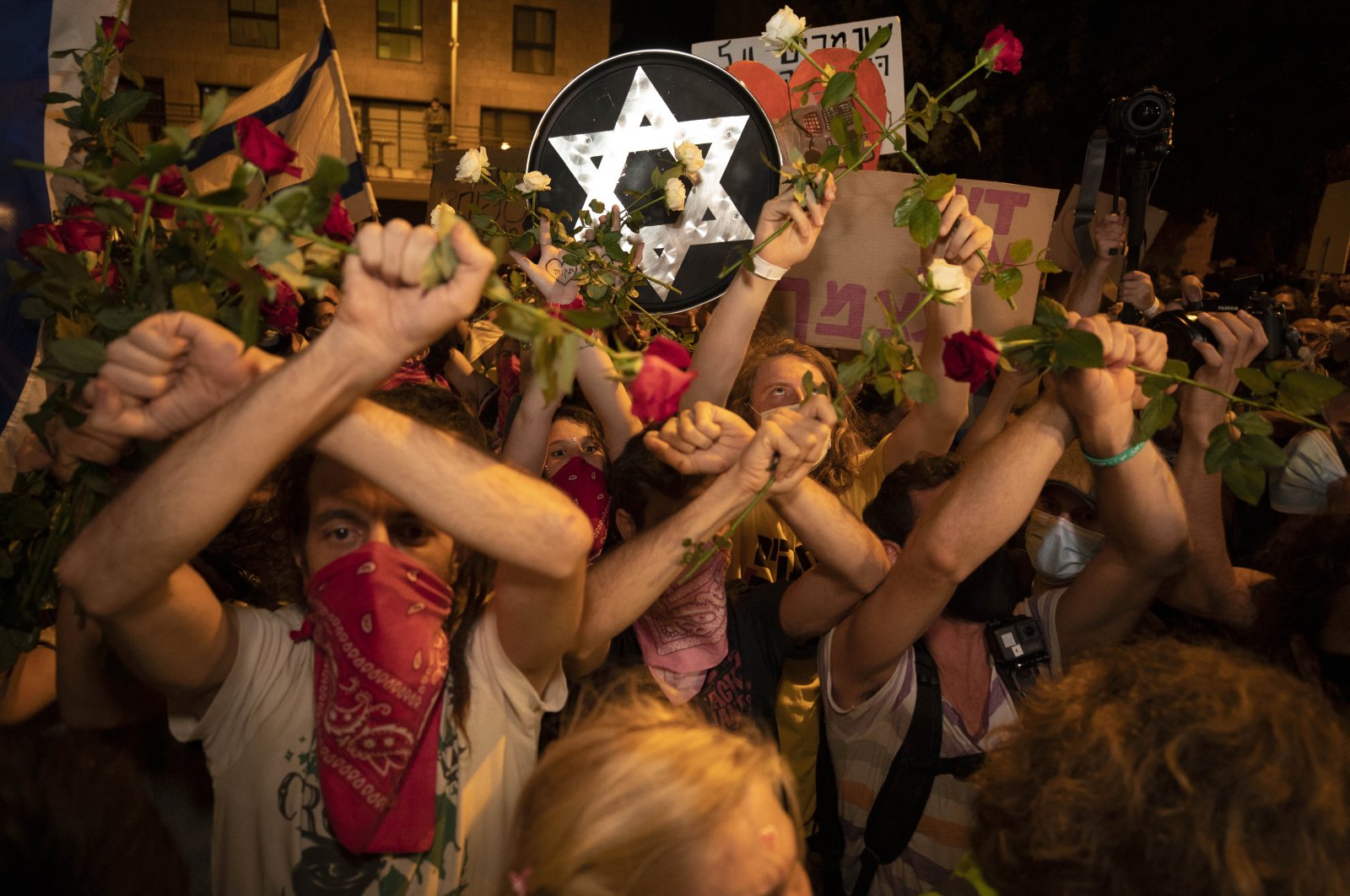 Israeli protesters hold flowers and chant slogans during a demonstration against Israeli Prime Minister Benjamin Netanyahu near the prime minister's residence in Jerusalem, Aug. 15, 2020. (AP Photo)