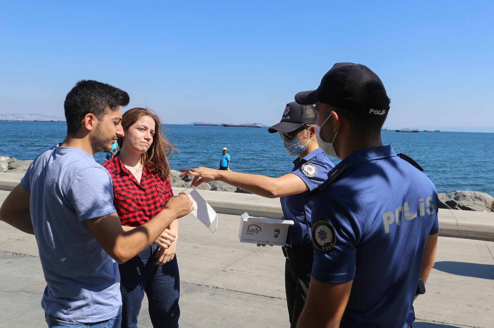 Police officers hand out masks to a couple walking on Bakırköy coastline without a mask, Istanbul, Turkey, Aug. 11, 2020. (AA Photo)