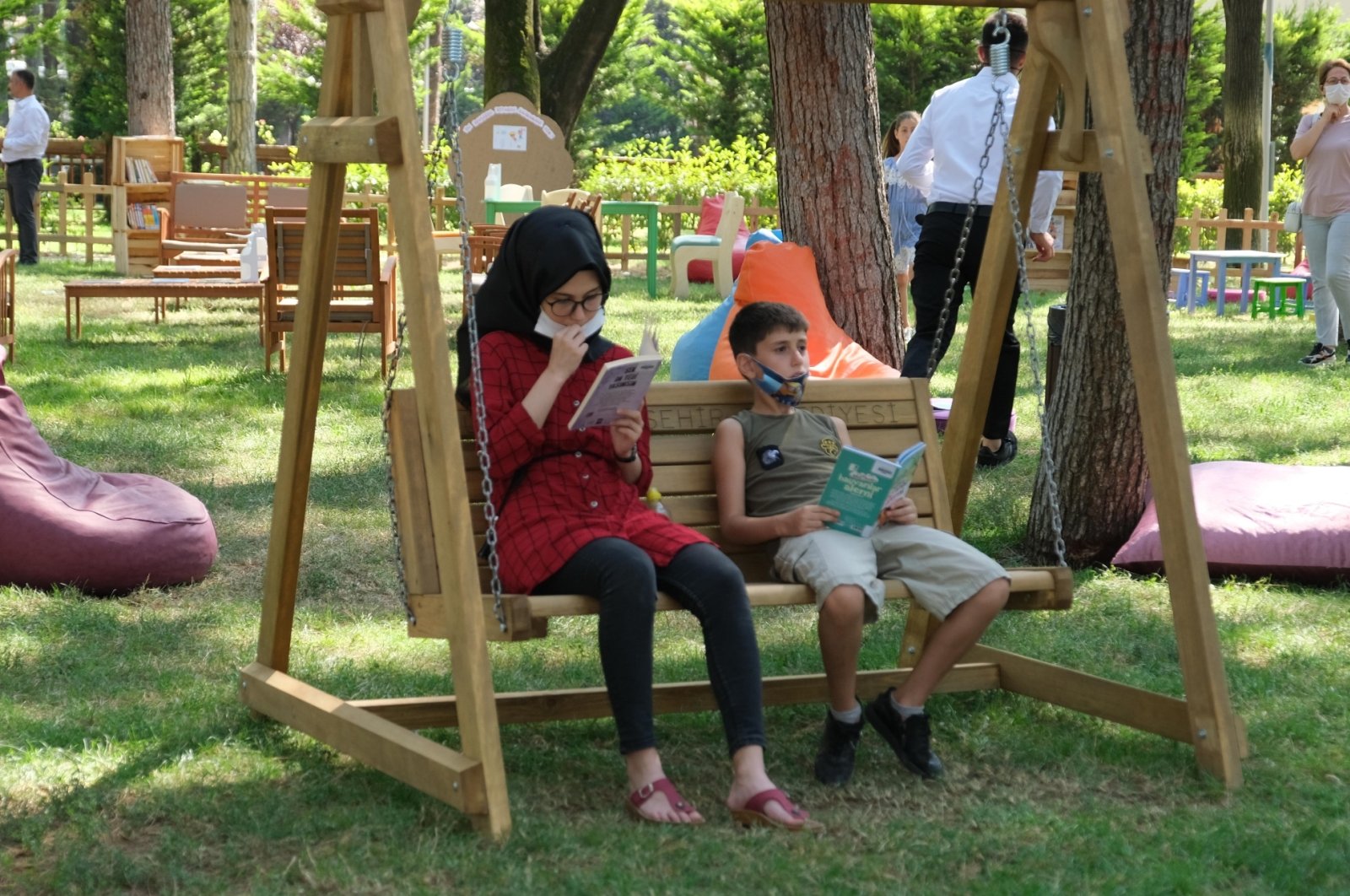 A girl and a boy sitting on a swing read books at the outdoor library, in Bursa, northwestern Turkey, Aug. 19, 2020. (AA Photo)
