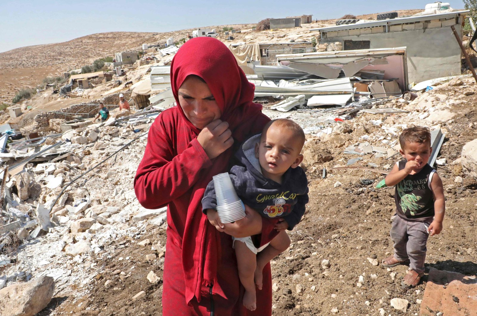 A Palestinian woman walks carrying a baby past wreckage of mobile homes built with European Union funding and destroyed by Israeli forces in the village of Mufagara south of Yatta near Hebron, as they were purportedly built without Israeli authorization, occupied West Bank, Sept. 11, 2019. (AFP Photo)