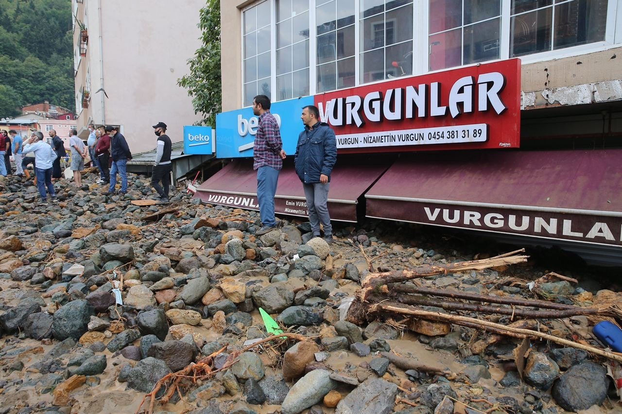 People stand on earth and debris brought on by the floods, with several shops buried deep beneath in the background, Giresun, Turkey, Aug. 23, 2020. (AA Photo)