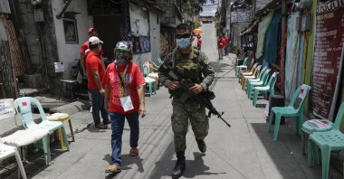 An army soldier walks with a volunteer as they wait for relief goods to be distributed and placed on chairs outside homes during a continuing enhanced community quarantine to prevent the spread of the coronavirus in Quezon City, Metro Manila, Philippines, May 4, 2020. (AP Photo)
