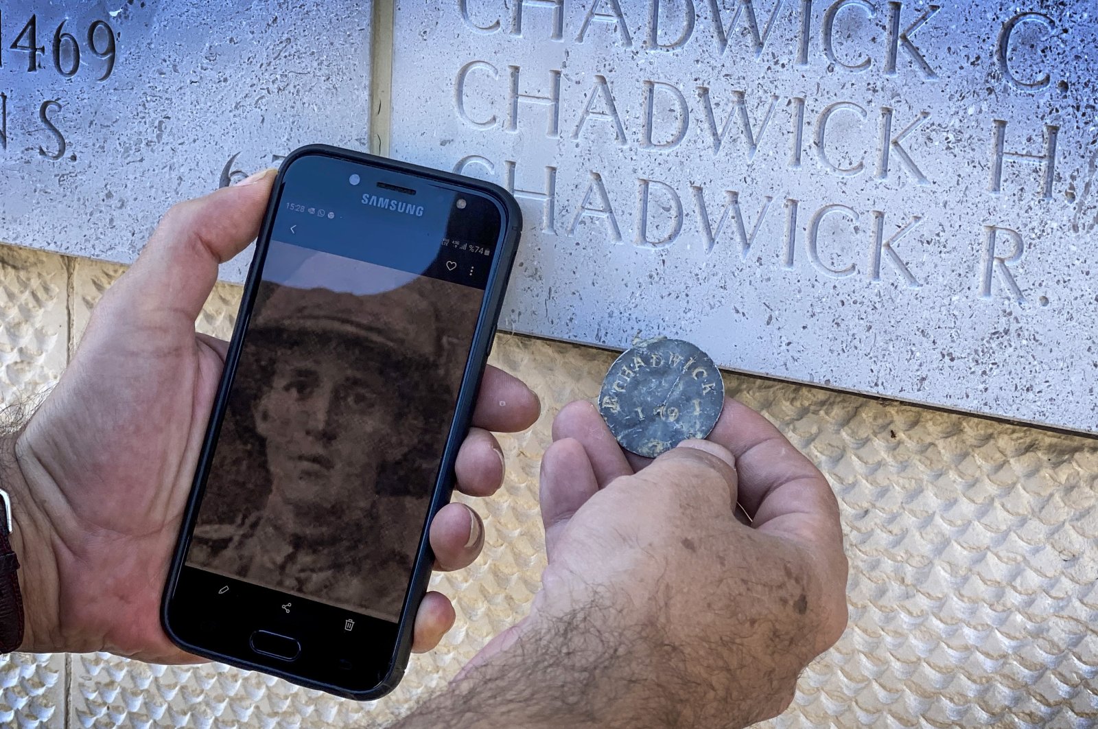 Seyit Ahmet Sılay shows the dog tag and photo of British soldier Robert Chadwick in front of a monument with the name of the soldier inscribed on it, in Çanakkale, western Turkey, Aug. 24, 2020. (AA Photo)