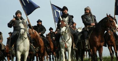 A still shot from the Turkish series "Resurrection: Ertuğrul" depicting Ertuğrul (C) and other Turkish heroes (Alps) riding horses and holding the iconic flag of the Kayı tribe.