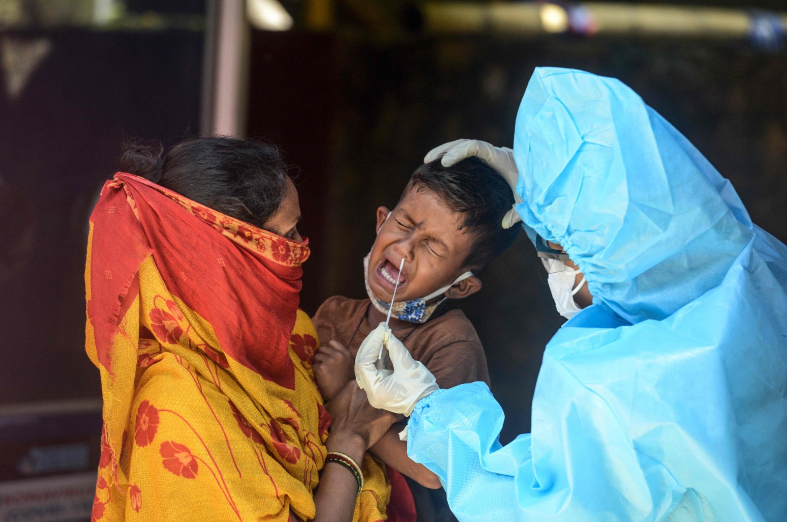 A health worker (R) wearing a Personal Protective Equipment (PPE) suit collects a swab sample from a child for a Rapid Antigen Test (RAT) for COVID-19 at a testing center in Siliguri, India, Aug. 26, 2020. (AFP Photo)