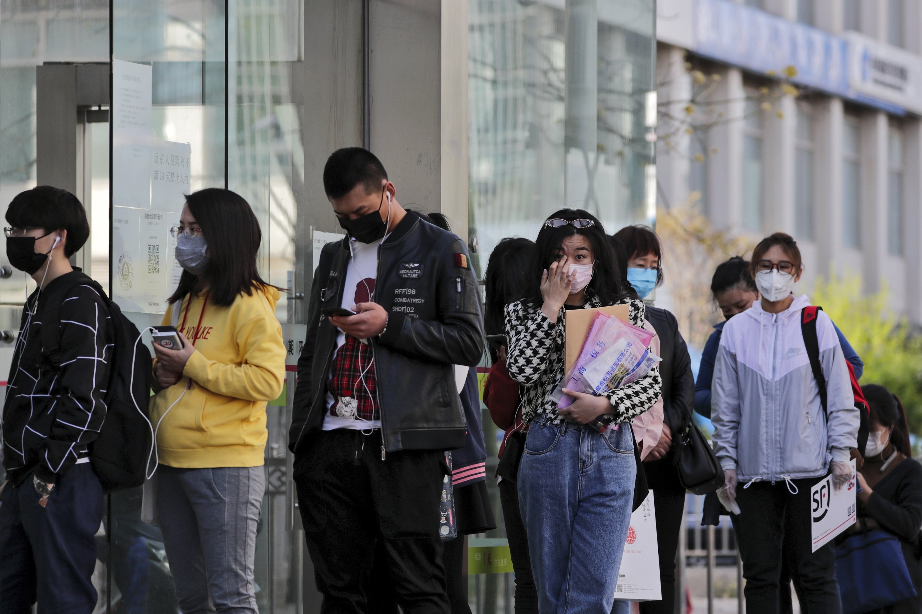 People wearing protective face masks wait in a queue to get temperature checks and a health code before entering an office building in Beijing, April 20, 2020. (AP Photo)