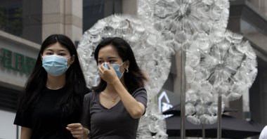 A woman adjusts her mask worn to protect against the coronavirus as they walk past a public art sculpture depicting giant spores in Beijing on Wednesday, Aug. 26, 2020. (AP Photo)
