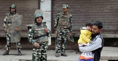 A man carrying a child walks past security forces in a riot-affected area, New Delhi, Feb. 27, 2020. (REUTERS Photo)