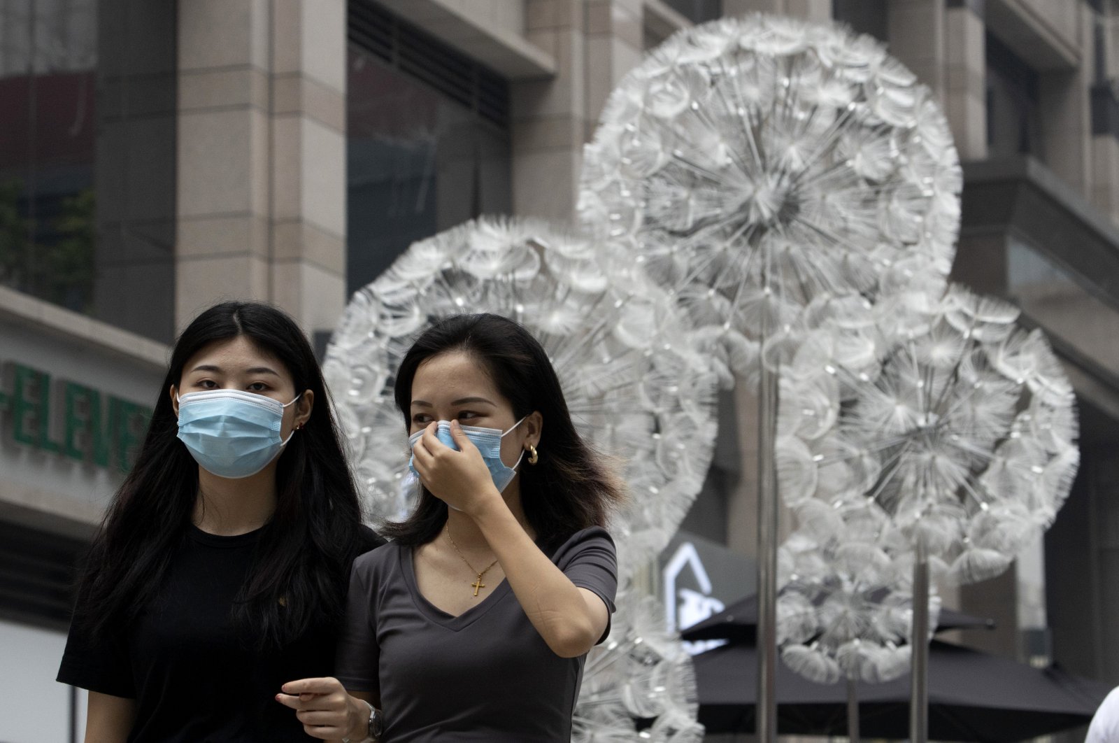 A woman adjusts her mask worn to protect against the coronavirus as they walk past a public art sculpture depicting giant spores in Beijing on Wednesday, Aug. 26, 2020. (AP Photo)