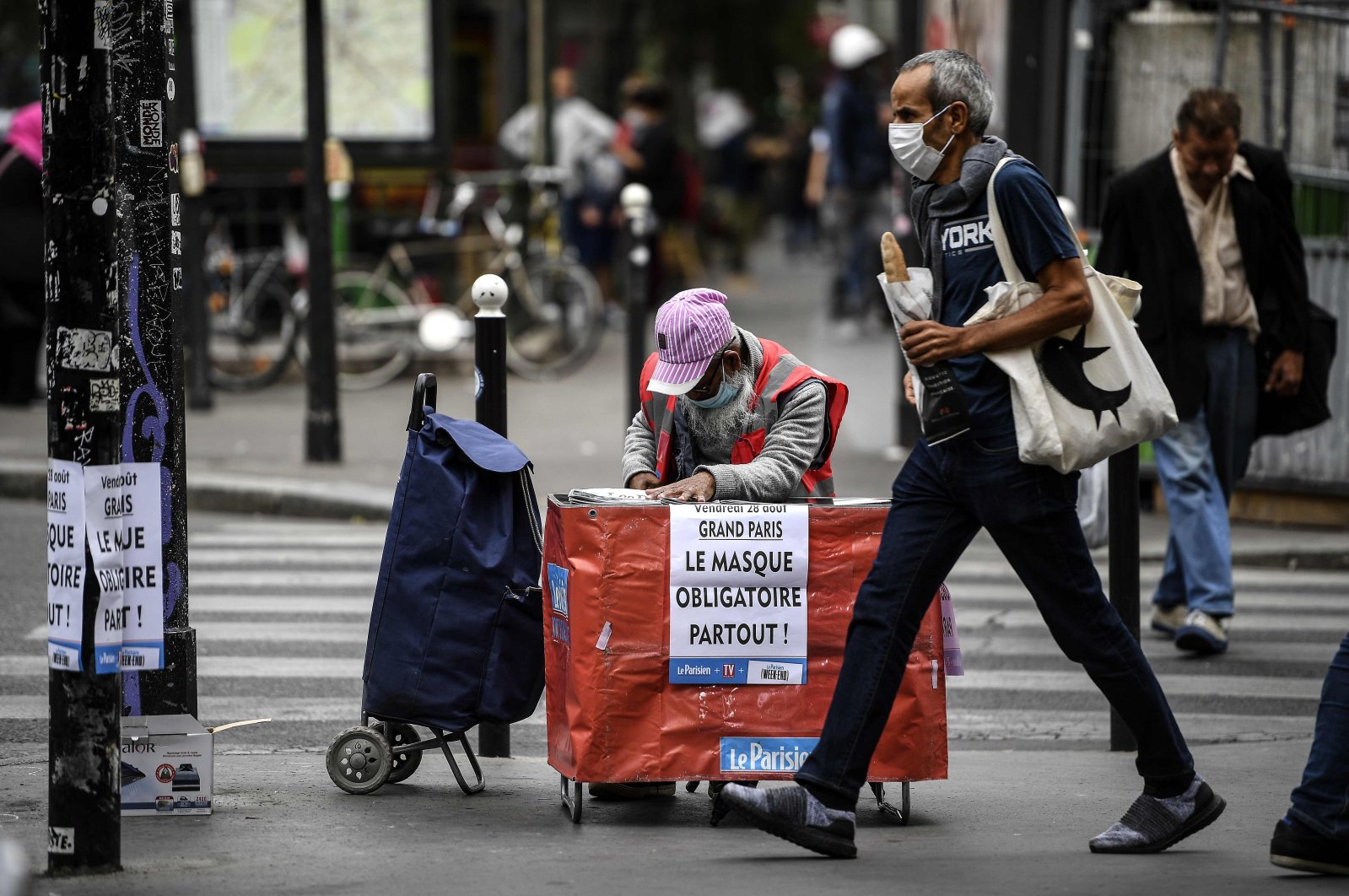 A placard hangs on the side of a newspaper stand reading, 'Paris The Mask Is Mandatory Everywhere' as the vendor wearing a protective face mask waits for customers in Paris on Aug. 28, 2020. (AFP Photo)