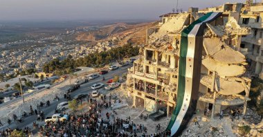 An aerial view of Syrians gathering for a demonstration by the ruins of a building that was hit in prior bombardment and adorned with a giant flag of the Syrian opposition, in the town of Ariha in the opposition-held northwestern Idlib province, Aug. 28, 2020. (AFP Photo)