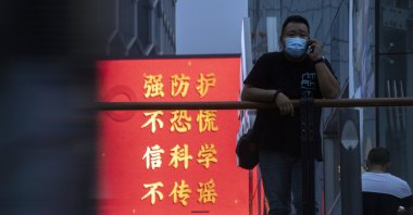 A man wearing a mask to protect from the coronavirus stands near government propaganda against the pandemic which reads "Strengthen Protection, Don't Panic, Believe in Science, Don't spread rumors" in Beijing, Aug. 30, 2020. (AP Photo)