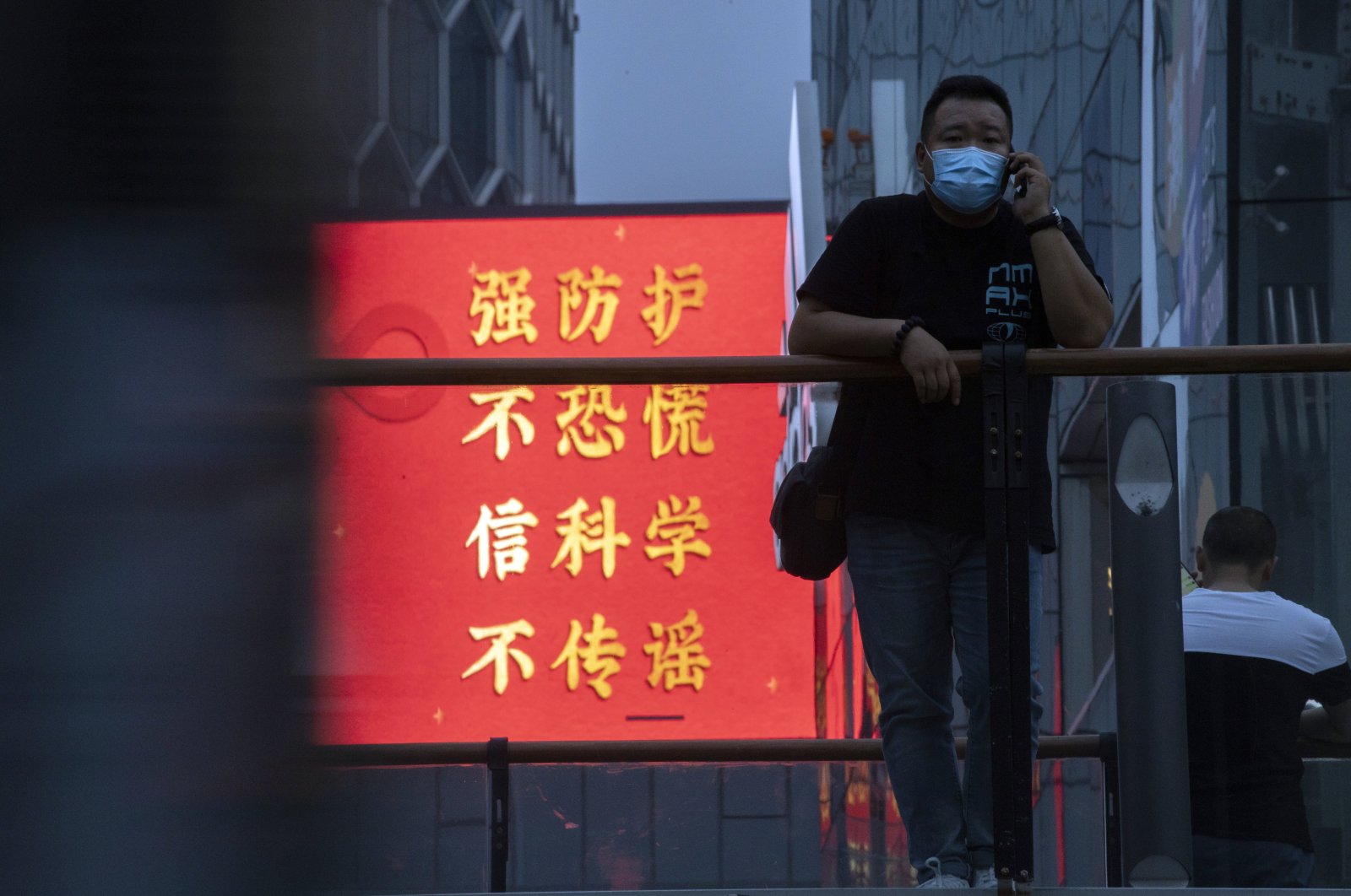 A man wearing a mask to protect from the coronavirus stands near government propaganda against the pandemic which reads "Strengthen Protection, Don't Panic, Believe in Science, Don't spread rumors" in Beijing, Aug. 30, 2020. (AP Photo)