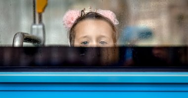 A little girl peers from behind a window bus upon arriving with kindergarten colleagues for a day of joint activities in Bucharest, Romania, Wednesday, Aug. 19, 2020. (AP Photo)