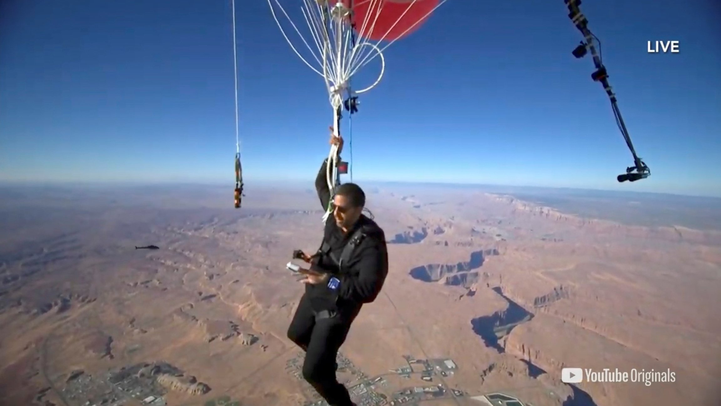 Extreme performer David Blaine hangs with a parachute under a cluster of balloons during a stunt to fly thousands of feet into the air, in a still image from video taken over Page, Arizona, U.S., Sept. 2, 2020.  (David Blaine handout via Reuters)