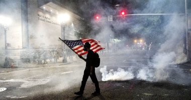 A Black Lives Matter protester carries an American flag as teargas fills the air outside the Mark O. Hatfield United States Courthouse, Portland, Oregon, July 21, 2020. (AP Photo)