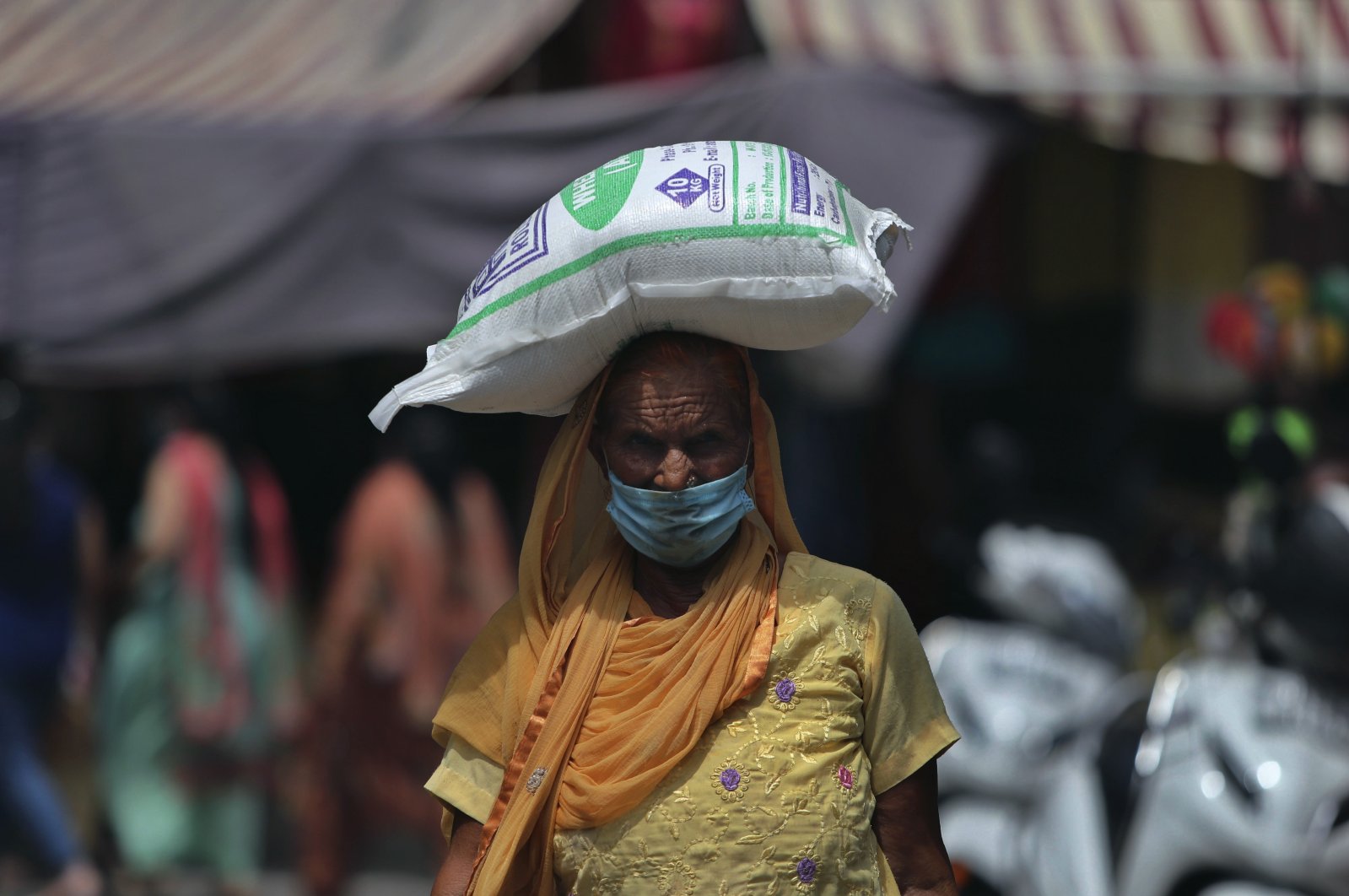 An Indian woman wearing face mask as a precaution against the coronavirus walks carrying a bag of flour on her head  in Jammu, India, Thursday, Aug 6, 2020. (AP Photo)