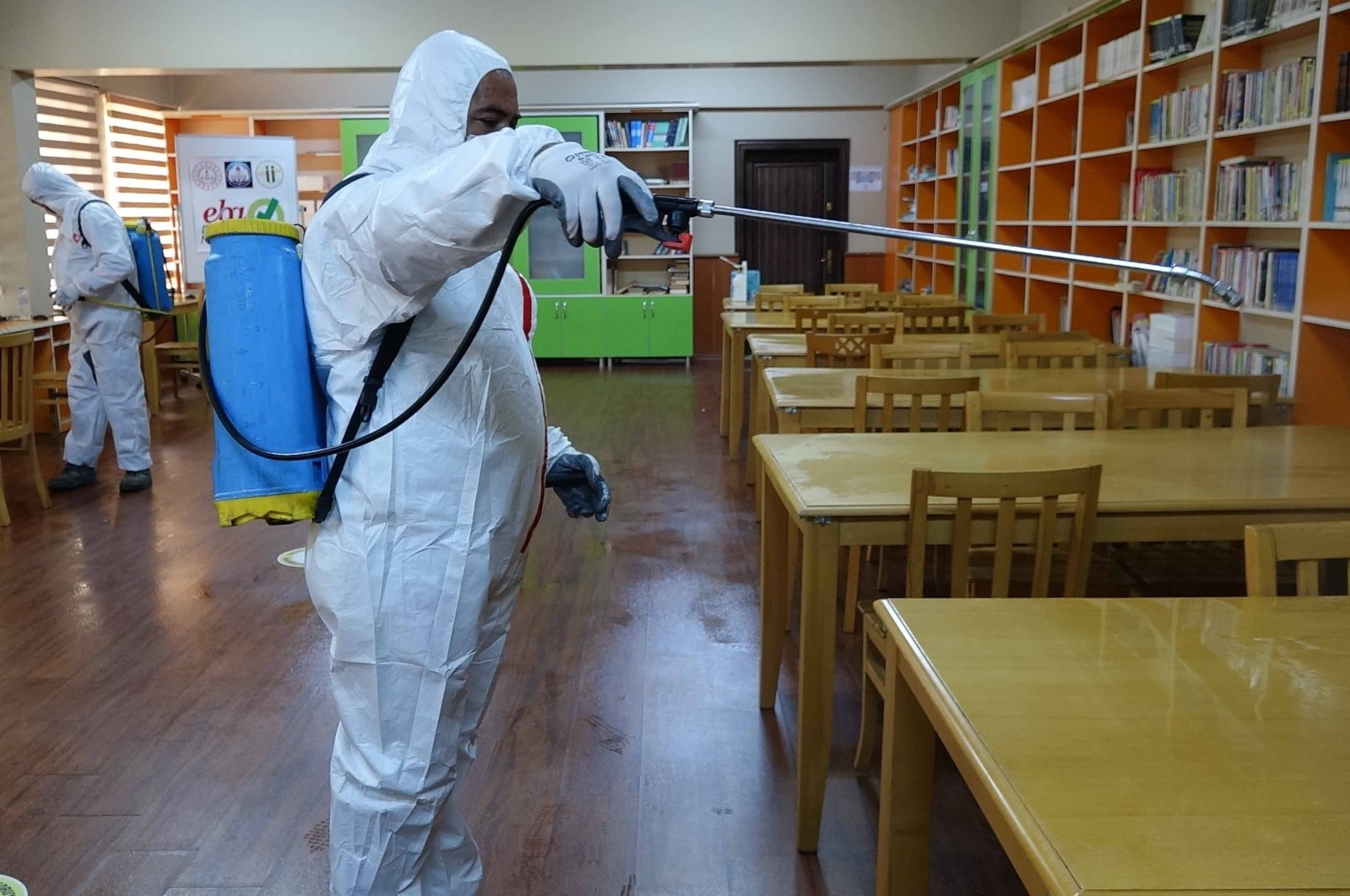 A man dressed in personal protective equiment (PPE) disinfects tables and bookshelves at a school in Adana province, southern Turkey, Sept. 3, 2020. (IHA Photo)