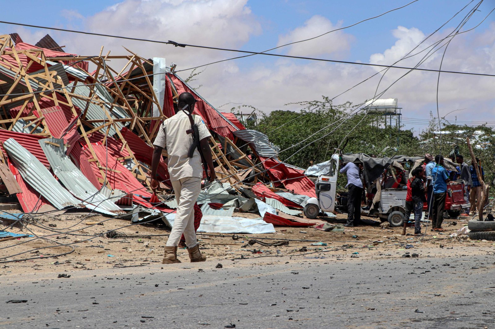 A Somali police officer patrols (L) as bystanders gather at the site of a suicide car bombing that targeted a European Union vehicle convoy in Mogadishu, Somalia, Sept. 30, 2019. (AFP Photo)