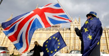 In this file photo, an anti-Brexit demonstrator waves a British flag alongside a European Union flag outside the Houses of Parliament in London, March 28, 2018. (AFP Photo)