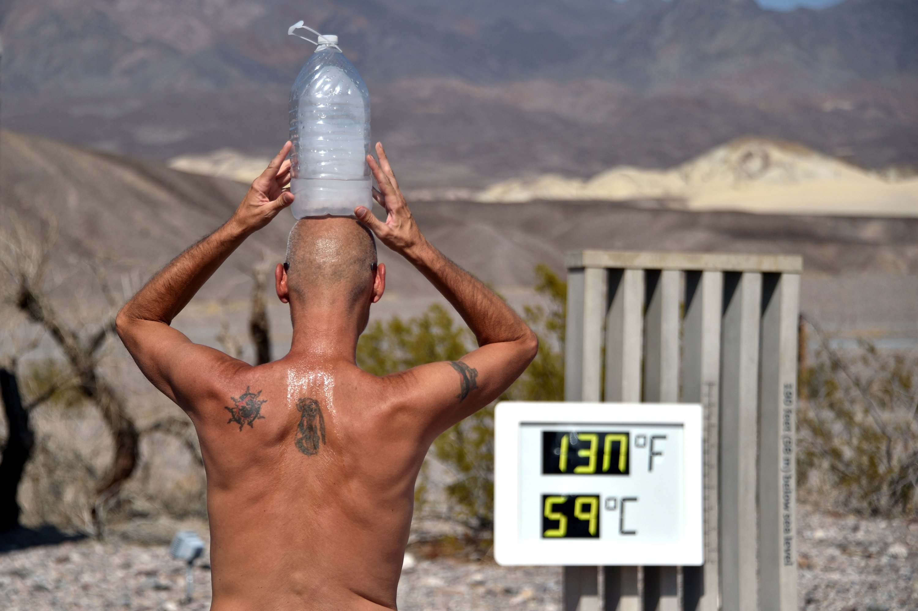 Steve Krofchik of Las Vegas keeps cool with a bottle of ice on his head as the unofficial thermometer reads 130 degrees Fahrenheit (54.4 Celsius), with a mechanical fault on the display which causes the numbers to render incorrectly, at the Furnace Creek Visitors Center in Death Valley, California, U.S. Aug. 17, 2020. (REUTERS Photo)