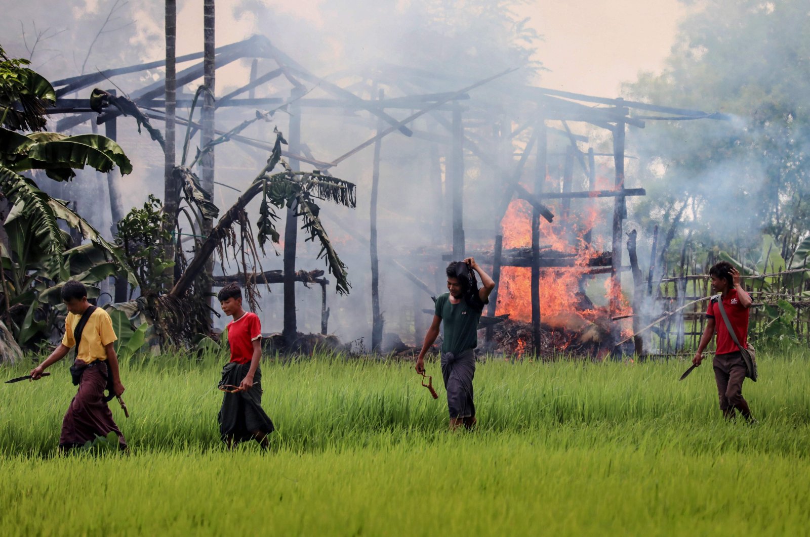 Unidentified men carry knives and slingshots as they walk past a burning house in Gawdu Tharya village near Maungdaw in Rakhine state in northern Myanmar, Sep. 7, 2017. (AFP Photo)