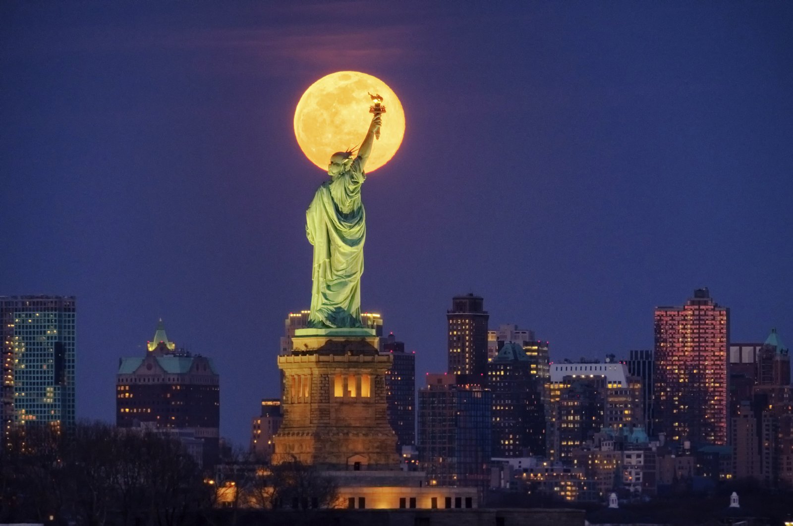 The full moon rises behind the Statue of Liberty in New York, March 9, 2020. (AP Photo)