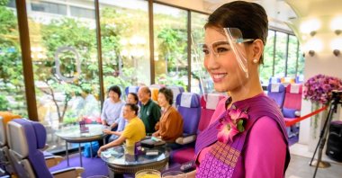 This picture taken on September 10, 2020 shows a Thai Airways flight attendant wearing a face shield as she serves drinks at a pop-up air-plane-themed restaurant at the airline's headquarters in Bangkok. (AFP Photo)