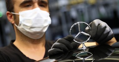An employee wearing a face mask attaches a Mercedes emblem as he works on an S-class car at the Mercedes plant in Sindelfingen, Germany, April 30, 2020. (AP Photo)