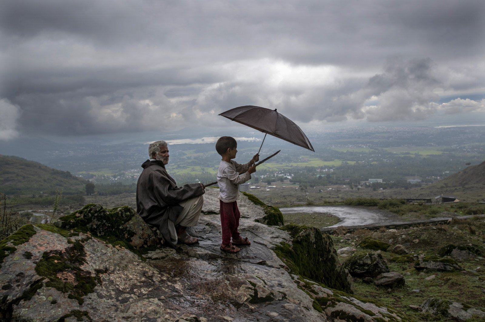 A Kashmiri villager with his grandson keeps watch over their cattle from a hillock on the outskirts of Srinagar, Indian-controlled Kashmir, Aug. 31, 2020. (AP Photo)