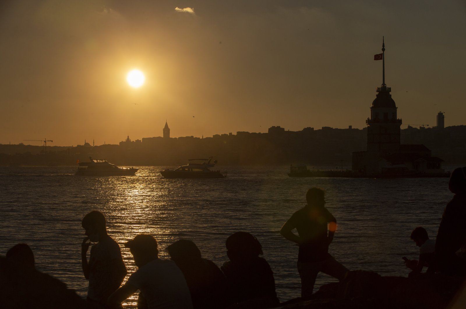 People enjoy themselves near the Bosporus backdropped by the Galata Tower and the Maiden's Tower at sunset in Istanbul, Aug. 23, 2020. (EPA Photo)