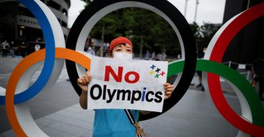 A demonstrator wearing a face mask holds a sign to protest against the Tokyo 2020 Olympic Games, in Tokyo, Japan on July 24, 2020. (Reuters Photo)