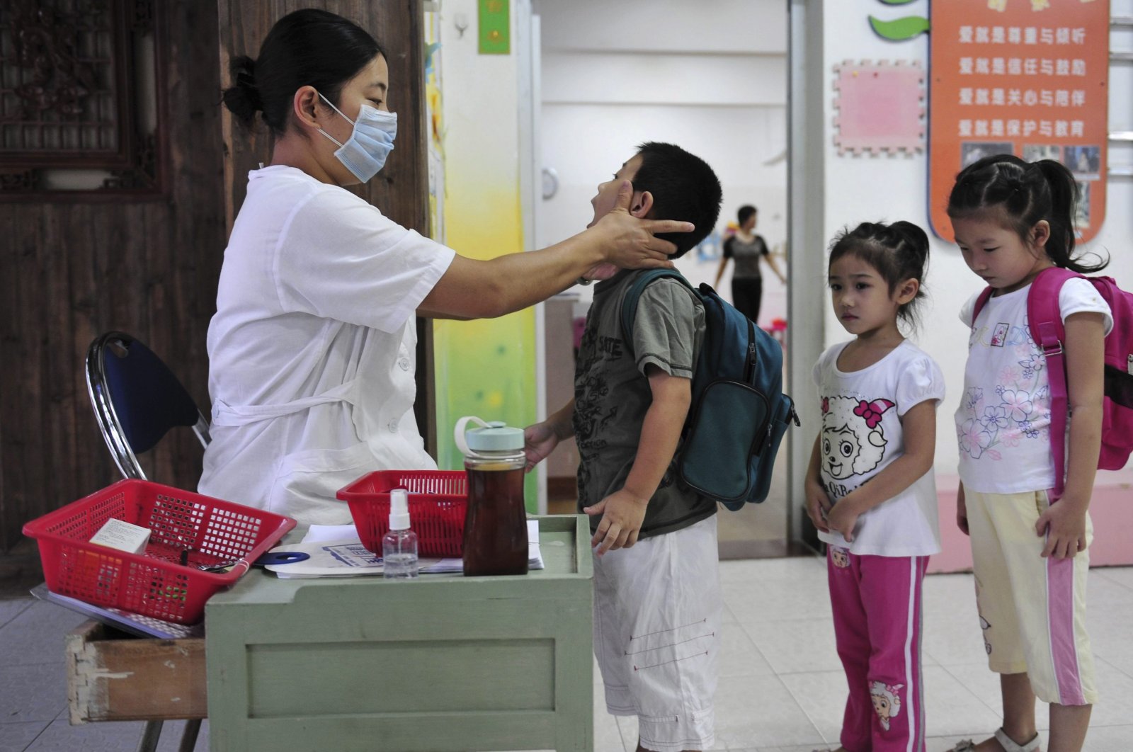 In this file photo, a teacher checks a child for symptoms of fever at a kindergarten as part of the routine precautions against swine flu (H1N1) in Fuzhou, southeast China's Fujian province, Sept. 22, 2009.